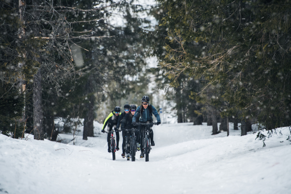 A group of young mountain bikers riding on road outdoors in winter.