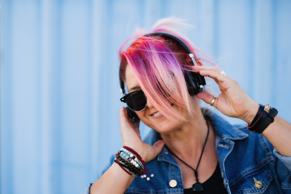 Portrait of senior woman with purple pink hair and sunglasses standing against blue background.