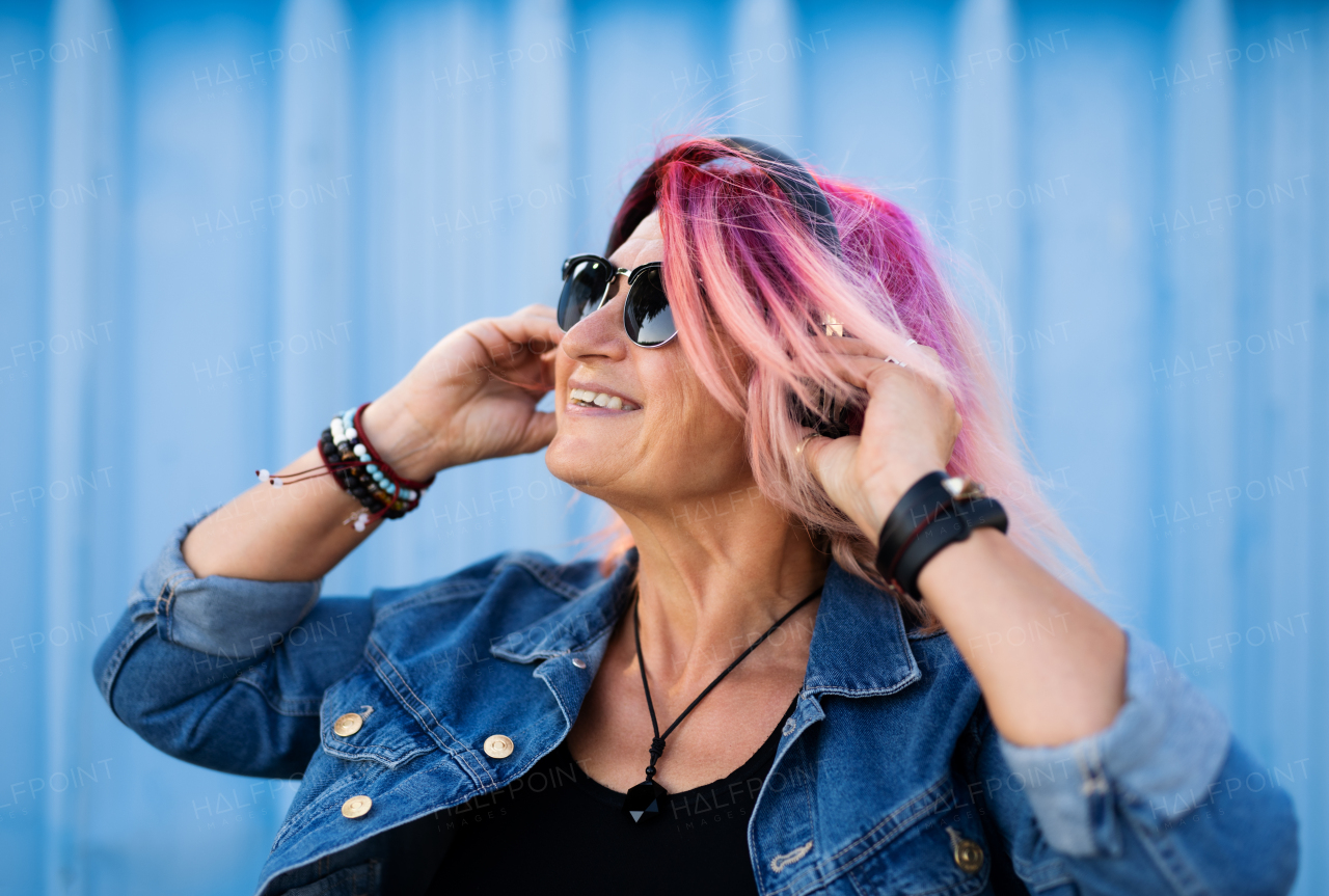 Portrait of senior woman with purple pink hair and sunglasses standing against blue background.