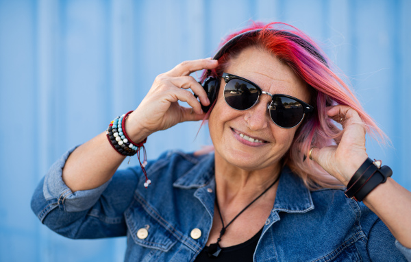 Portrait of senior woman with purple pink hair and sunglasses standing against blue background.