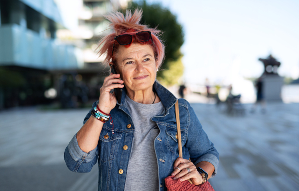 Portrait of senior woman with purple pink hair and smartphone walking outdoors in city or town.