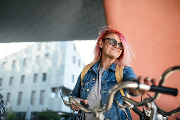 Portrait of senior woman with purple pink hair and bicycle standing outdoors in city or town.