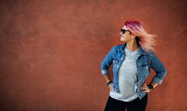 Portrait of senior woman with purple pink hair standing against brown background.