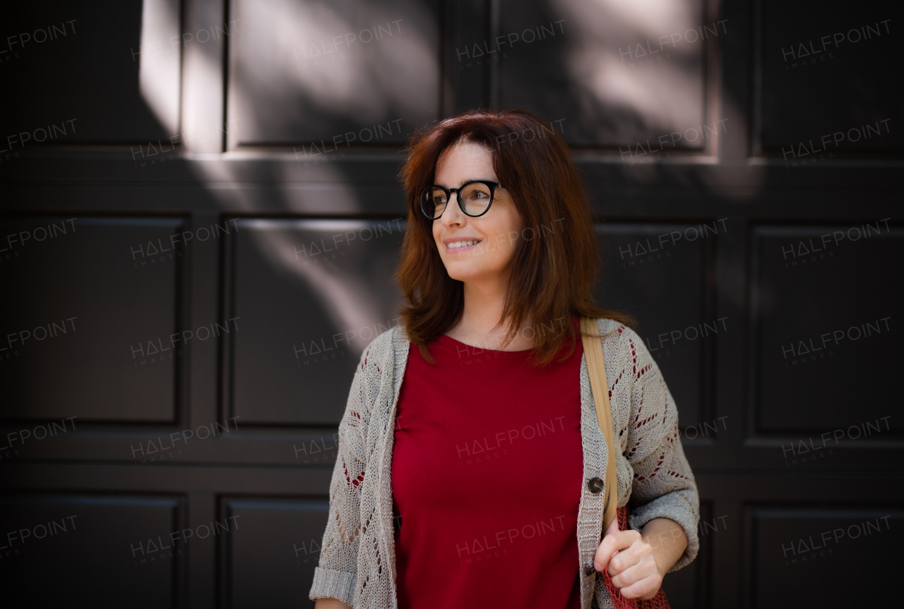 Portrait of mature woman standing outdoors in city or town, dark background.