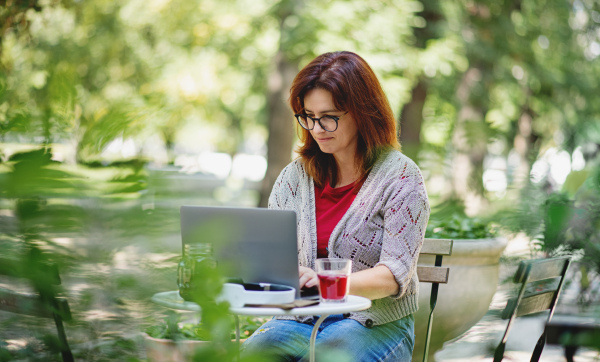 Mature woman with laptop sitting at the table outdoors city cafe, working.