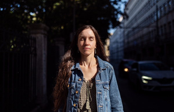 Portrait of mature woman standing outdoors in city or town park at dusk.