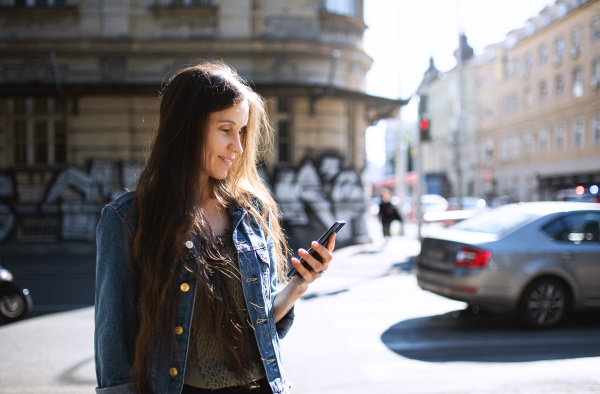 Portrait of mature woman with smartphone outdoors in city or town park, walking.