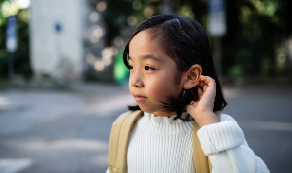 Portrait of small Japanese girl with backpack walking outdoors in town. Copy space.