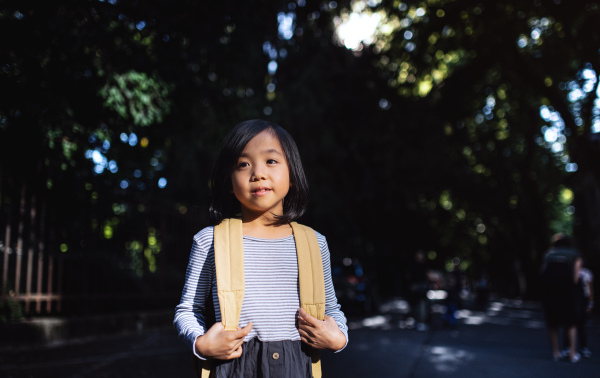 Portrait of small Japanese girl with backpack walking outdoors in town. Copy space.