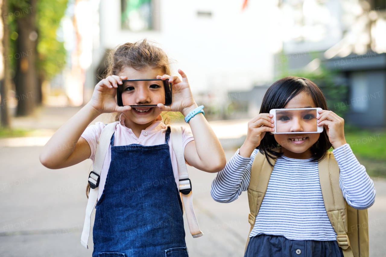 Small girls holding smartphone in front of eyes outdoors in town, having fun.