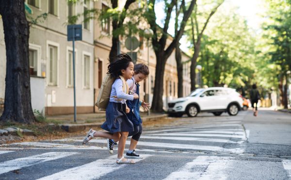 Cheerful small girls crossing street outdoors in town, coronavirus concept.