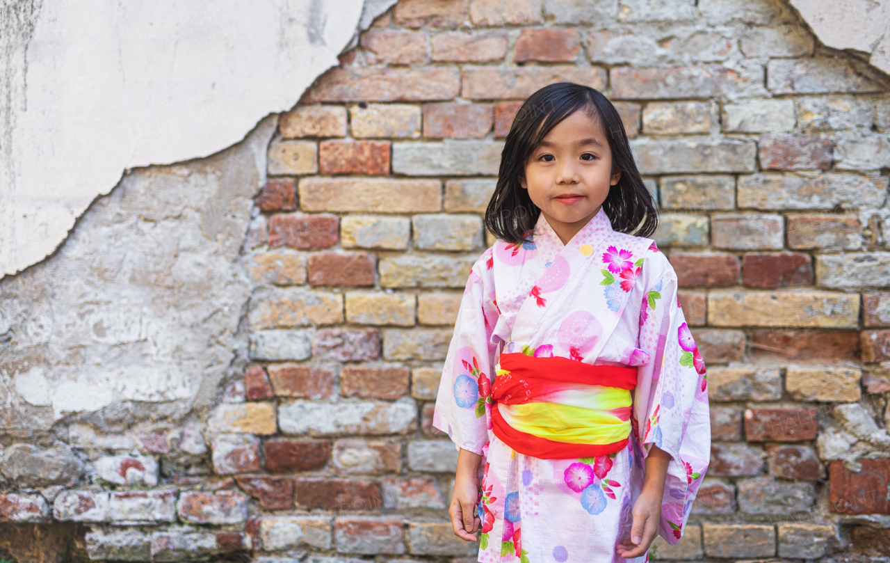 Portrait of small Japanese girl wearing kimono outdoors in town, looking at camera.