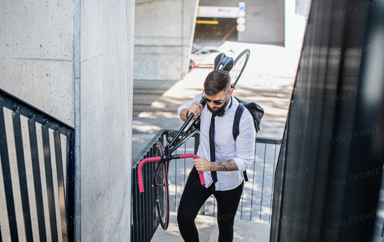 Portrait of young man commuter with headphones and bicycle walking outdoors in city.