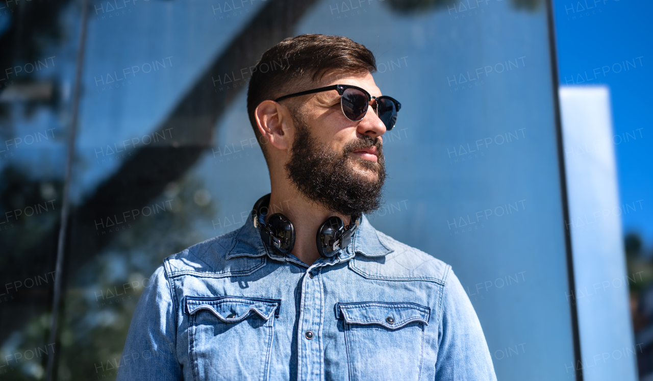 Portrait of young man with headphones standing outdoors in city.