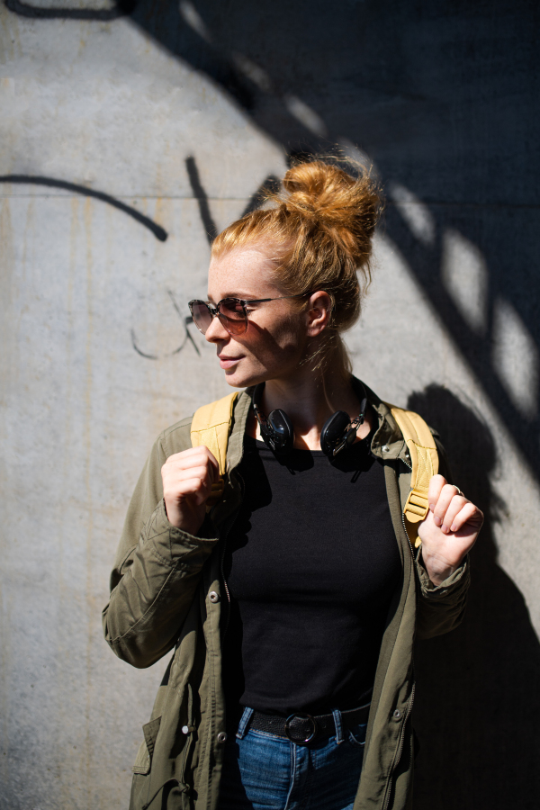 Front view portrait of happy young woman with red hair outdoors in town, wearing sunglasses.