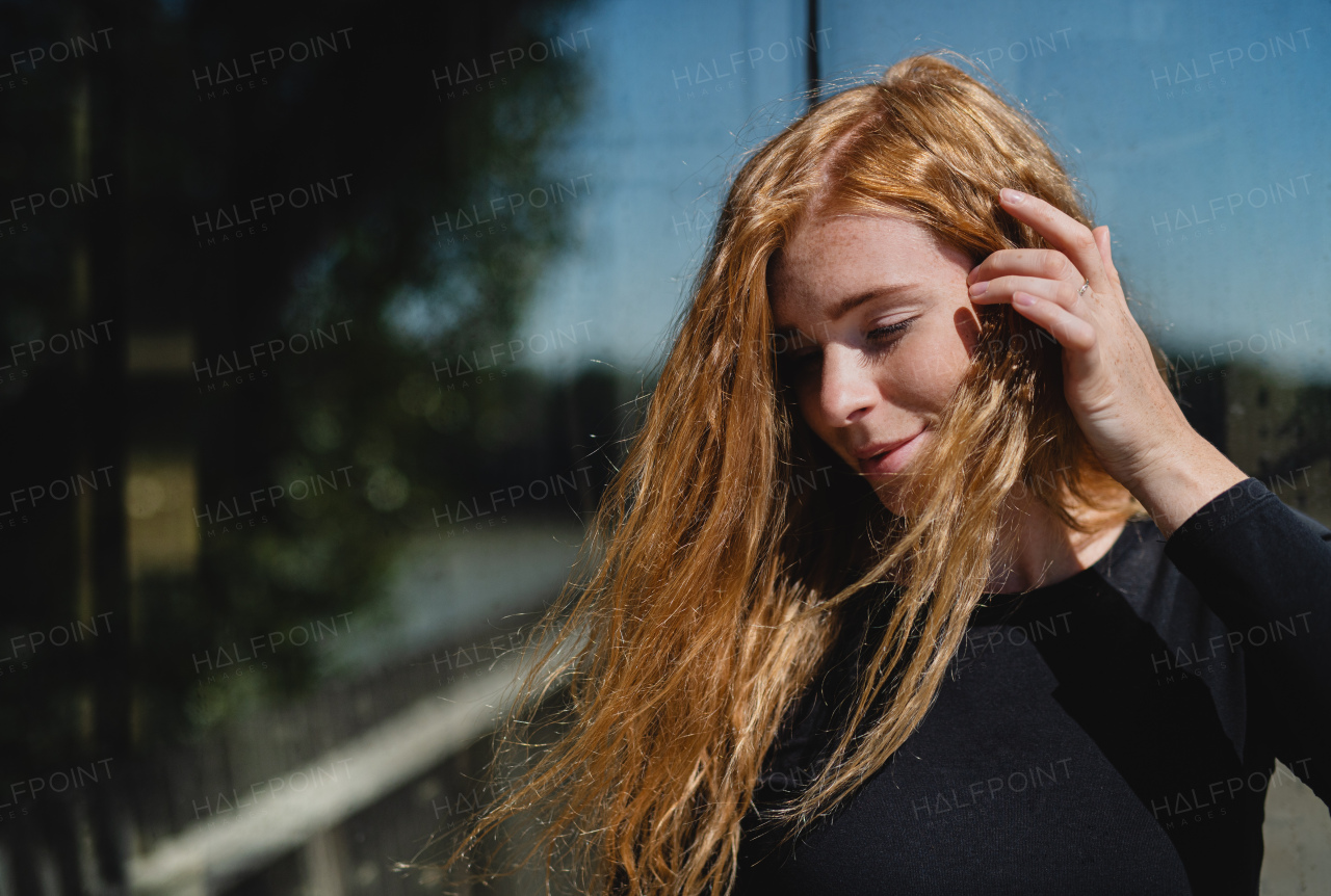 Portrait of young woman with red hair and closed eyes outdoors in town. Copy space.