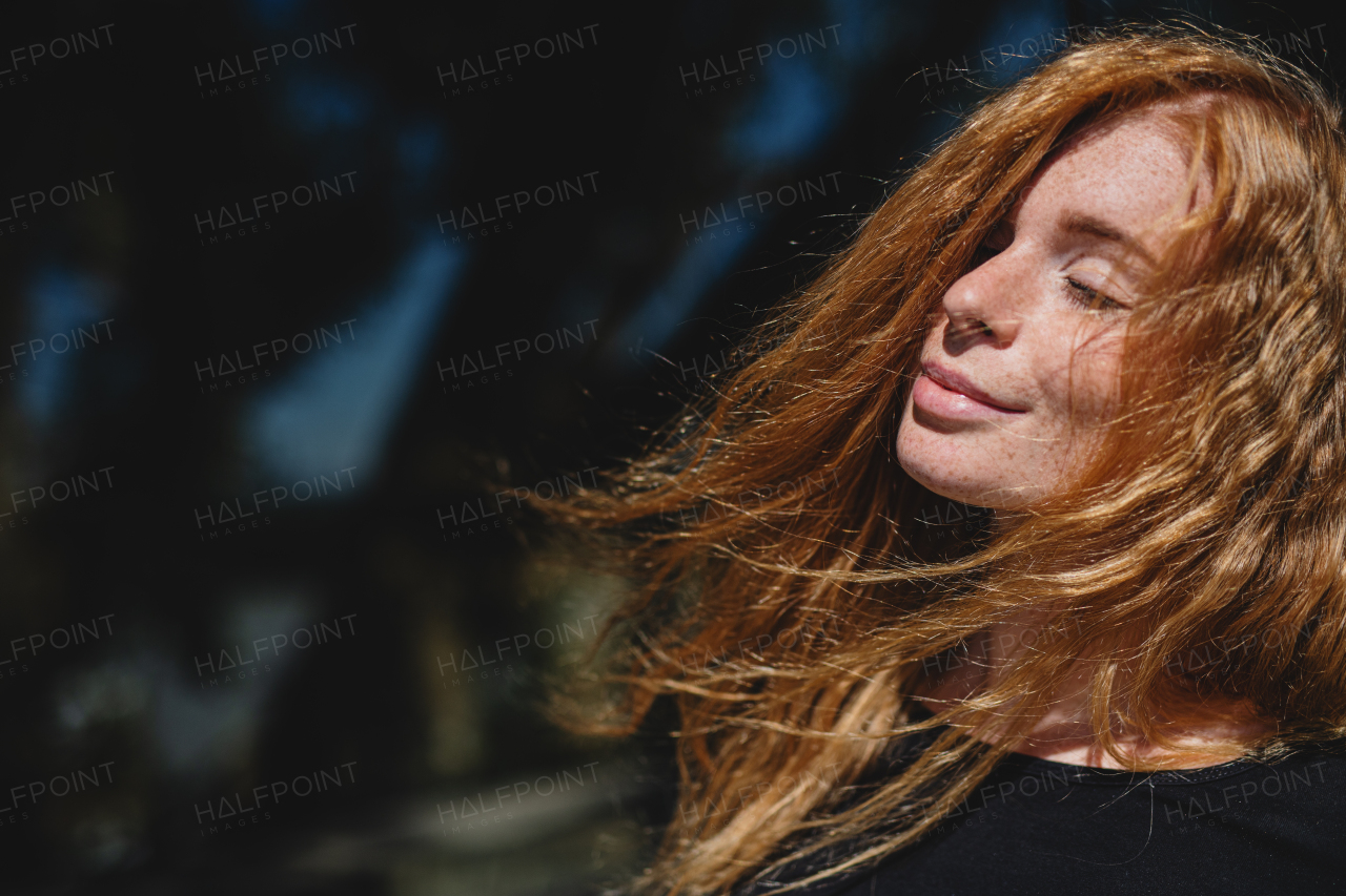 Portrait of young woman with red hair and closed eyes outdoors in town. Copy space.