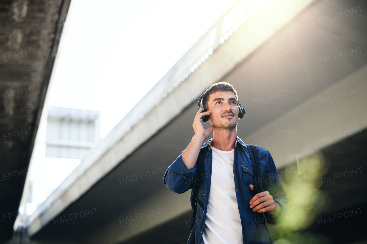 Low-angle view of young attractive man with headphones standing outdoors in city. Copy space.