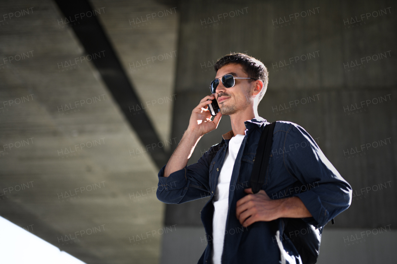 Portrait of young attractive man with headphones and smartphone walking outdoors in city.