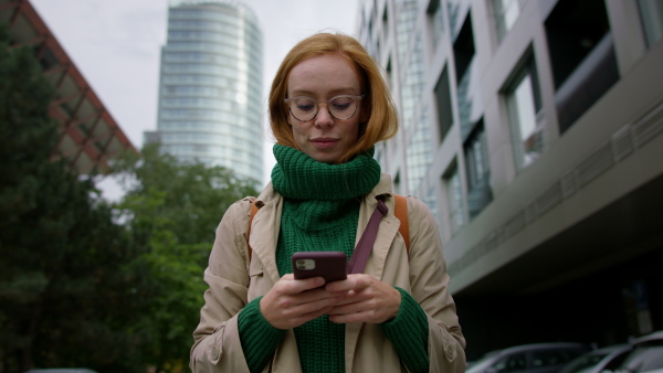 A mid adult woman using smartphone and walking in town.