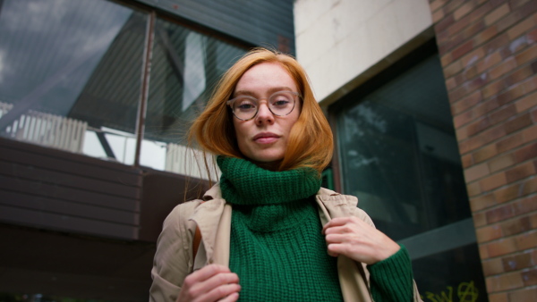 A low angle view of young woman turning and looking at camera in winter in street.