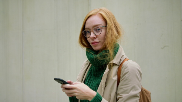 A young woman using smartphone and walking in street in autumn.