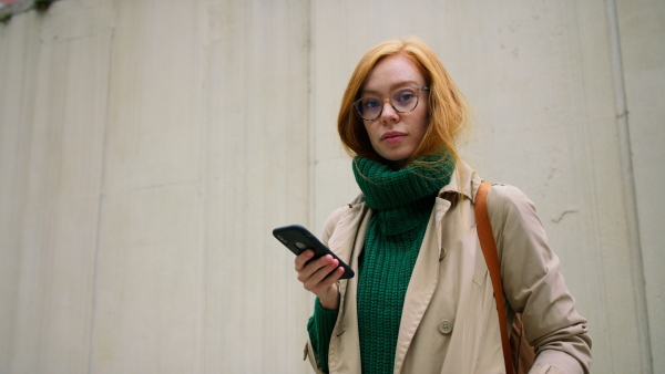 A young woman using smartphone and walking in street in autumn.