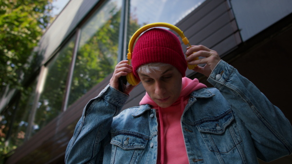 A low angle view of cool young man with headphones outdoors in town, looking at camera.