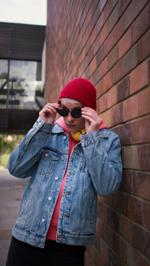 A vertical footage of cool young man with headphones and smartphone outdoors in town, putting on sunglasses.