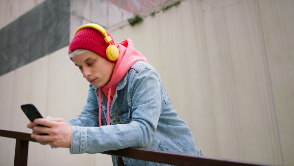 A cool young man with headphones and smartphone outdoors in town, looking at camera.