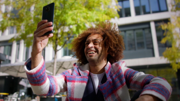 A low angle view of cool multiracial mid audlt man having vide call with smartphone outdoors in town