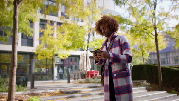 A cool multiracial mid audlt man commuter walking with smartphone outdoors in town