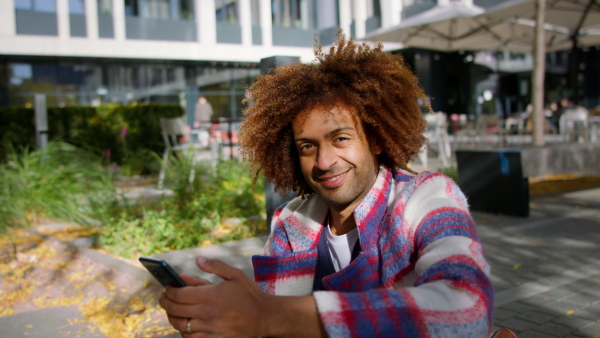 A cool multiracial mid audlt man with smartphone outdoors in town