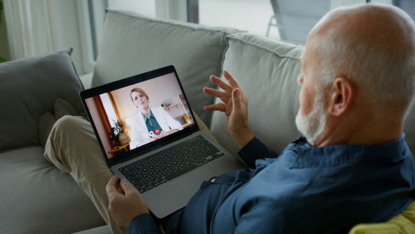 A senior man lying on sofa and having video call with his doctor.