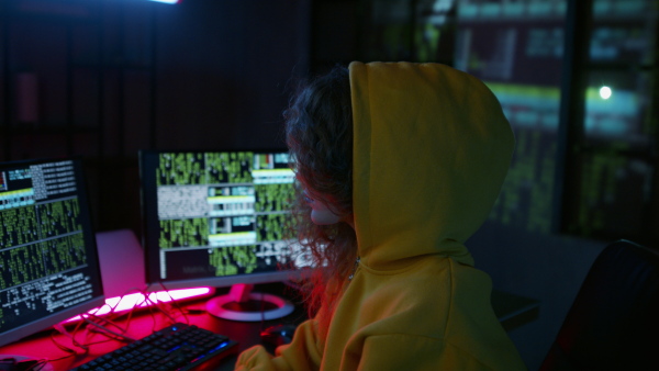 A young woman hacker by computer in the dark room at night, cyberwar concept.