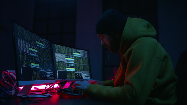 A young man hacker by computer in the dark room at night, cyberwar concept.