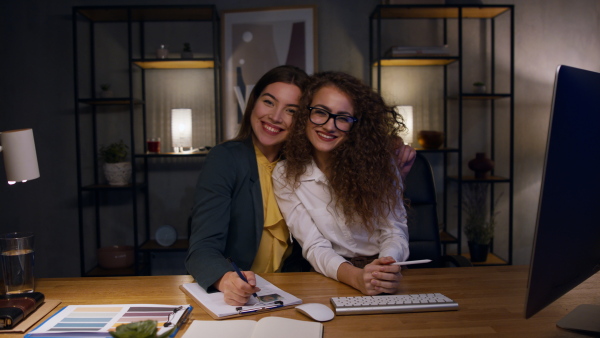 Two female office assistants smiling at camera. Dark ambient.