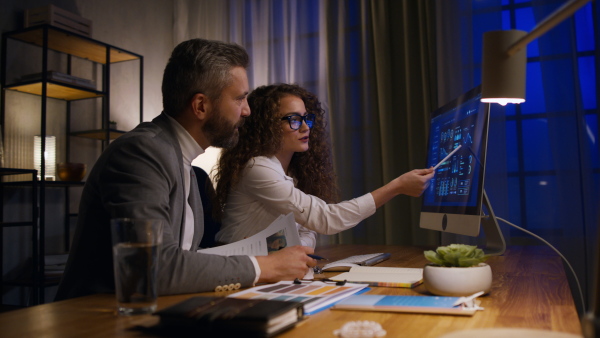 Young woman and her colleague working in office during evening, consulting something.