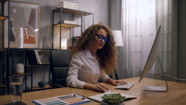 Young woman wearing glasses, working on computer in her home office.