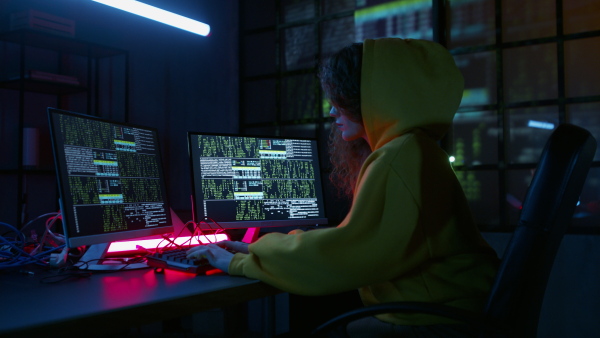 A young woman hacker by computer in the dark room at night, cyberwar concept.