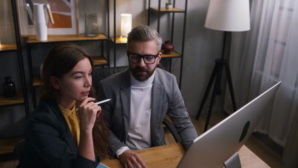 Young woman and her colleague working in office during evening, consulting something.