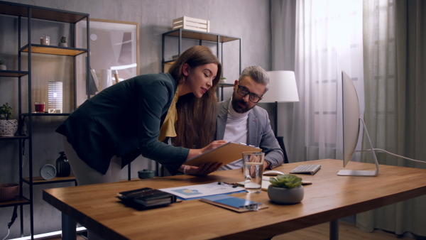 Young woman and her colleague working in office during evening, consulting something.