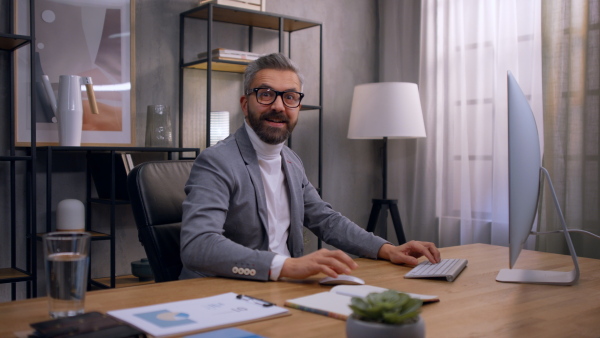 Happy and confident businessman pointing with finger at camera sitting at desk in office.