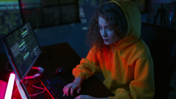 Young woman hacker coding on computer in dark ambient. Top view.