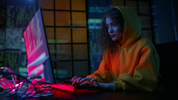 A young woman hacker by computer in the dark room at night, cyberwar concept.