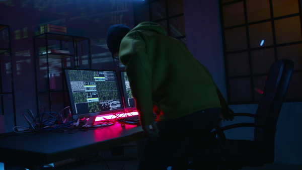 A young man hacker by computer in the dark room at night, cyberwar concept.