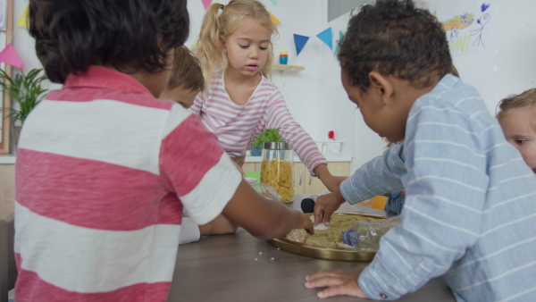 A pre school teacher with multiracial group of children sitting at table and playing indoors in nursery