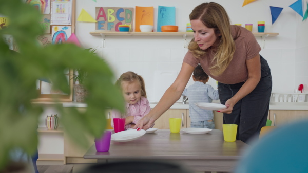 A pre school teacher setting the table for lunch indoors in nursery.