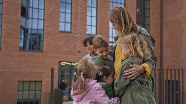 A pre school teacher hugging with small children during walk outdoors in town.