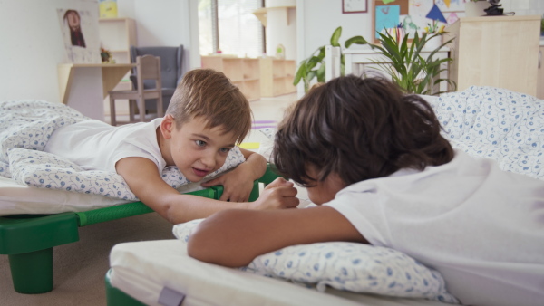 Preschool children in a pajamas lying in beds ready for nap indoors in nursery school.